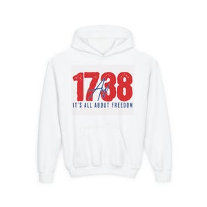 Può includere: Felpa con cappuccio bianca con grafica frontale. La grafica presenta il numero "1738" in rosso, con una sovrapposizione blu "Ay!" e il testo "IT'S ALL ABOUT FREEDOM" in blu.