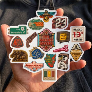 May include: A collection of colorful stickers with various designs and text. Designs include a race car number, a vintage television, a pair of scissors, and phrases like "The Great Divide" and "Paid Time Off."