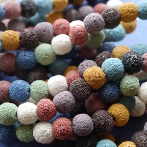May include: A close-up of a strand of colorful lava rock beads. The beads are round and have a porous texture. The colors include white, blue, green, yellow, brown, and purple.