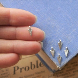 May include: Five silver triangle charms with a textured surface. The charms are small and have a hole at the top for attaching to jewelry.