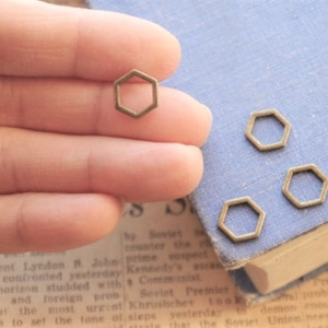 Puede incluir: Cuatro anillos hexagonales de metal de color dorado antiguo. Los anillos tienen un diámetro de aproximadamente 1,25 cm y un acabado liso ligeramente texturizado.