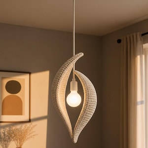 May include: A woven pendant light fixture with a teardrop design. The light fixture is white and cream-colored, with a bulb in the center. The light hangs from a white ceiling mount. The background includes a framed picture and a vase.