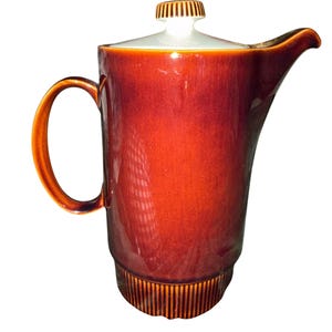 May include: A tall ceramic coffee pot featuring a deep reddish-brown glaze with a subtle crackle finish. The vessel has a cylindrical body, a curved handle, a pointed spout, and a white lid topped with a small, ribbed, brown knob handle.