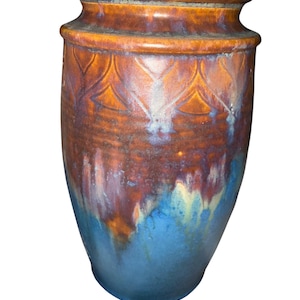 May include: A cylindrical ceramic vase featuring a thick, rounded rim and a tapered base. The upper portion displays a warm, earthy brown glaze with a subtle embossed petal pattern, transitioning into a vibrant, deep blue glaze at the bottom.