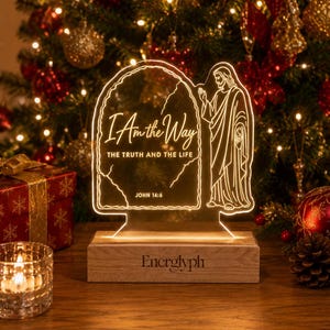 May include: An illuminated acrylic sign featuring a line drawing of a figure and the text I Am the Way THE TRUTH AND THE LIFE JOHN 14:6. The clear acrylic panel is mounted on a rectangular wooden base with the brand name Energlyph engraved on it.