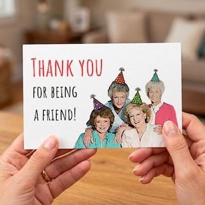 May include: A greeting card with the text "Thank You For Being A Friend!" in red and black. The card features a cartoon illustration of four women wearing party hats. The women are smiling and appear to be celebrating.