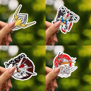 May include: A collection of four die-cut vinyl stickers featuring various robot head designs. One sticker shows a yellow head, another displays a white, blue, and red robot with the text RX-78, while others feature detailed mechanical head illustrations.