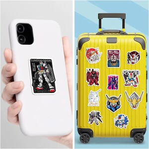 May include: A white smartphone with a rectangular Gundam Origin sticker and a yellow rolling suitcase covered in various Gundam robot stickers, including head portraits, full-body figures, and Japanese text characters on a bright yellow surface.