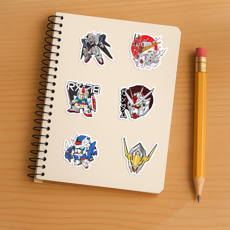May include: A spiral-bound notebook featuring six distinct Gundam-themed stickers. The designs include various robot figures, a head portrait with Japanese text, and the label RX-78. The stickers are arranged in two columns on the off-white paper.