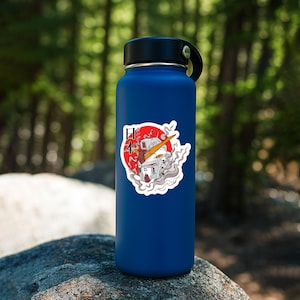 May include: A matte navy blue water bottle featuring a sticker of a white and orange robot head surrounded by swirling gray smoke against a red circular background with the Japanese characters 日本 printed in black on the left side.