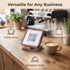 Puede incluir: Un soporte cuadrado de madera que sostiene un letrero blanco con un código QR negro y el texto "Jetzt digital nachreichen". La pantalla está rodeada de iconos y etiquetas para cafetería, tienda minorista y recepción, con una taza de café.