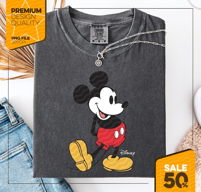 Pu&ograve; includere: T-shirt Comfort Colors grigio scuro con una grafica di Topolino sorridente. Mickey indossa pantaloncini rossi e scarpe gialle. Una collana d'argento con un ciondolo &egrave; sulla maglietta. La maglietta ha il logo Disney e l'etichetta Comfort Colors.