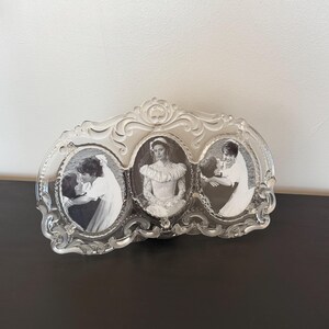 May include: A clear glass triple picture frame featuring an ornate, molded scrollwork border. The frame holds three oval-shaped black and white photographs, each depicting a person in a wedding dress and veil in various poses.