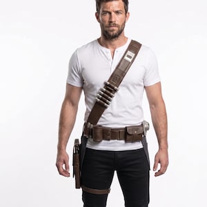 May include: A brown leather utility belt with multiple pouches, a holster, and a shoulder strap with silver-colored details. The belt is worn over black pants and a white Henley shirt. The belt has a leg strap.