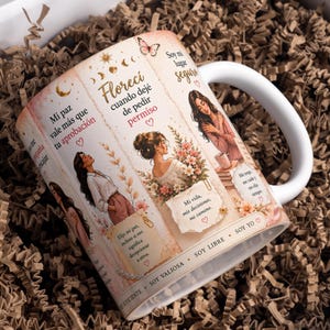 Puede incluir: Una taza de cerámica blanca con un diseño envolvente que muestra ilustraciones de mujeres, detalles florales, mariposas y símbolos celestiales. La taza incluye frases en español como 'Mi paz vale más que tu aprobación' y 'Florecí cuando dejé de pedir permiso'.