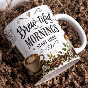 Op de afbeelding: Een witte keramische mok met de zwarte tekst Brew-tiful MORNINGS START HERE. Het ontwerp bevat illustraties van een koffiekop met latte art, koffiebonen, kaneelstokjes, witte bloemen en een klein bordje met de tekst Coffee House.