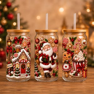 May include: Three clear glass tumblers with bamboo lids and clear straws. The first features a gingerbread bakery, the second a smiling Santa Claus, and the third a gingerbread person with a mug of hot cocoa, all decorated with festive holiday motifs.