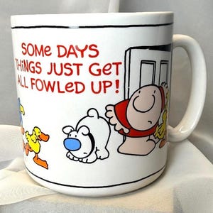 May include: A white ceramic mug featuring a cartoon illustration of a person, a small white dog with a blue nose, and yellow ducks. The text printed in red reads, "SOME DAYS THINGS JUST GET ALL FOWLED UP!" The mug has a handle on the right side.