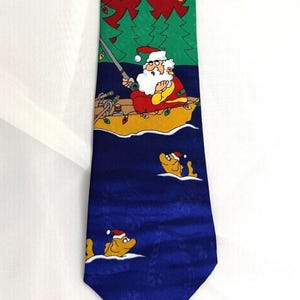 May include: A necktie featuring a holiday-themed graphic print. The design depicts Santa Claus in a yellow boat on dark blue water, fishing for yellow fish wearing Santa hats. The background includes green pine trees and a red sky with string lights.