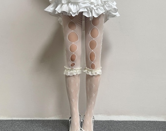 May include: White ruffled mini skirt paired with white fishnet tights featuring large circular cutouts along the legs and delicate lace trim at the knees. The ensemble is completed with white pointed-toe heels featuring a lace-up front detail.