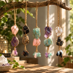 May include: Five hanging ornaments made of raw, multi-colored crystals encased in woven jute netting. Each ornament features two stacked, irregular stones in shades of pink, purple, black, green, and clear, finished with small crystal bead tassels.