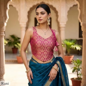 Peut inclure: Un chemisier sans manches magenta avec un motif brocart floral doré, doté d'une encolure en V et d'un ourlet pointu, associé à un sari bleu sarcelle uni avec une bordure dorée. L'ensemble comprend des boucles d'oreilles et des bracelets dorés.