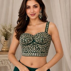 May include: A dark green sleeveless corset top featuring a sweetheart neckline and thick shoulder straps. The bodice is heavily embellished with geometric mirror work, silver metallic embroidery, and small white beads in a repeating pattern.