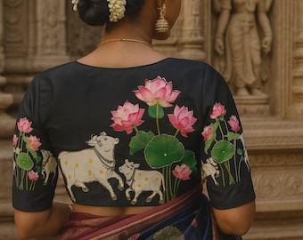 May include: A black blouse featuring hand-painted white cows with yellow spots and pink lotus flowers with green leaves on the back and sleeves, paired with a dark blue and maroon patterned sari featuring small tree and animal motifs.