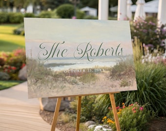 May include: A rectangular sign on a wooden easel featuring an impressionistic painting of a coastal beach scene with dunes and ocean waves. The text "The Roberts" is printed in a dark green script font, with "OCTOBER 15, 20XX" below it.