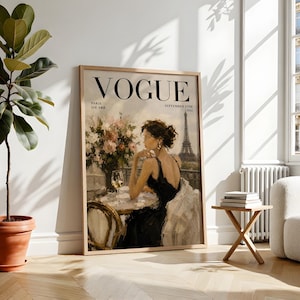May include: A framed Vogue magazine cover print. The artwork features a woman in a black dress seated at a table with a glass of wine, with the Eiffel Tower in the background. The magazine title and date are visible.