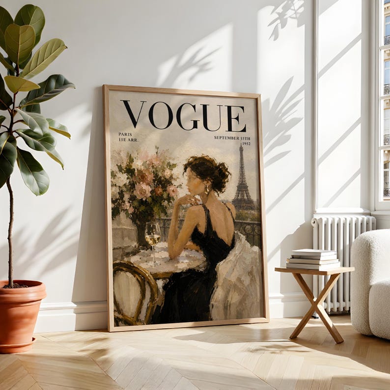 May include: A framed Vogue magazine cover print. The artwork features a woman in a black dress seated at a table with a glass of wine, with the Eiffel Tower in the background. The magazine title and date are visible.