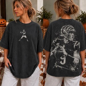 Op de afbeelding: Een antracietgrijs oversized t-shirt met een kleine afbeelding van een footballspeler op de borst en een grote, gedetailleerde afbeelding van een footballspeler met helm en bal op de achterkant, afgewerkt met een verwassen look.