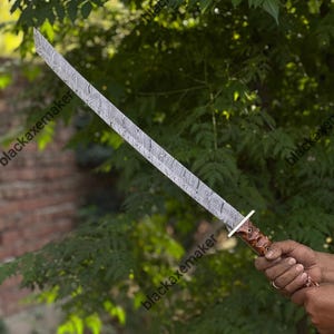 May include: A long sword featuring a distinctive wavy Damascus steel pattern on the blade, a silver-toned metal crossguard, and a textured brown wooden handle. The blade is straight with a sharp, angled tip and a visible metallic finish.