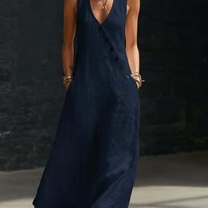 May include: A sleeveless, navy blue jumpsuit with a V-neckline and a button closure. The jumpsuit features two pockets and a flowing, wide-leg design. The fabric appears to be a lightweight linen or cotton blend.