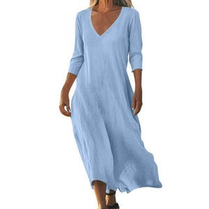 May include: A light blue, V-neck dress with three-quarter sleeves. The dress has a flowing, relaxed fit and falls to the mid-calf. The fabric appears to be a lightweight linen or cotton blend, suitable for warm weather.