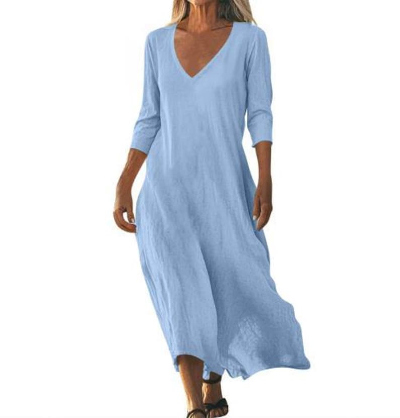 May include: A light blue, V-neck dress with three-quarter sleeves. The dress has a flowing, relaxed fit and falls to the mid-calf. The fabric appears to be a lightweight linen or cotton blend, suitable for warm weather.