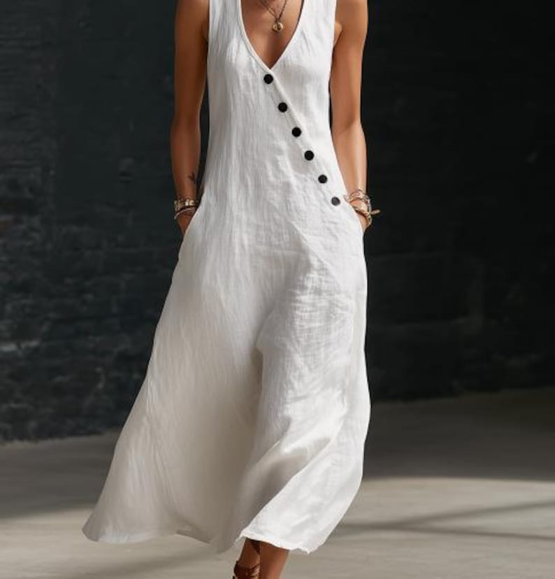 May include: A sleeveless white jumpsuit with a V-neckline and wide legs. The jumpsuit features a row of black buttons down the front and pockets. The fabric appears to be a lightweight linen or cotton blend, suitable for warm weather.