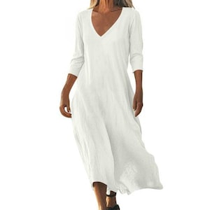 May include: A flowing, off-white dress with a V-neck and three-quarter sleeves. The dress has a relaxed fit and falls to the mid-calf. The fabric appears to be lightweight and textured, suitable for warm weather. The model is wearing black sandals.
