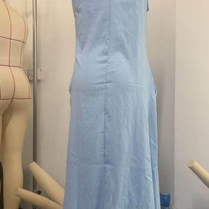 May include: A sleeveless, light blue dress displayed on a mannequin. The dress has a simple, flowing design with a V-neck and a slightly flared skirt. The fabric appears to be lightweight, suitable for warm weather.