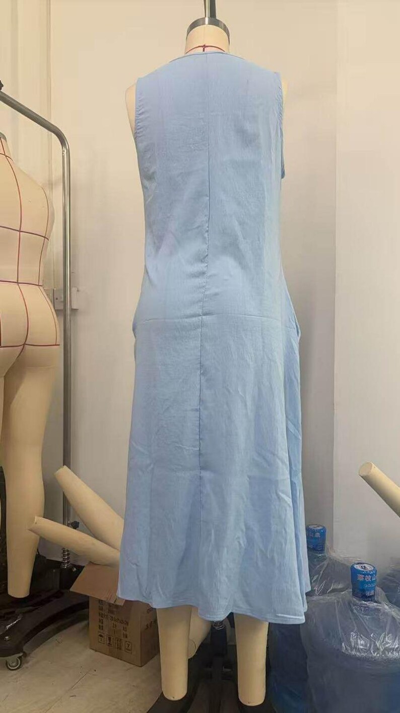 May include: A sleeveless, light blue dress displayed on a mannequin. The dress has a simple, flowing design with a V-neck and a slightly flared skirt. The fabric appears to be lightweight, suitable for warm weather.