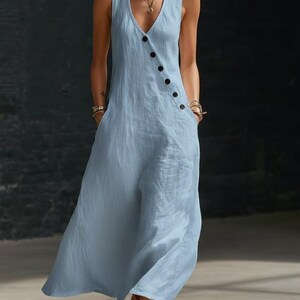 May include: A sleeveless, light blue jumpsuit with a V-neckline and a row of black buttons down the side. The jumpsuit has pockets and a flowing, wide-leg design, made of a soft, textured fabric.