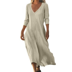 May include: A beige, V-neck dress with three-quarter sleeves. The dress has a loose, flowing silhouette and falls to mid-calf. The fabric appears to be a lightweight linen or cotton blend, suitable for warm weather.