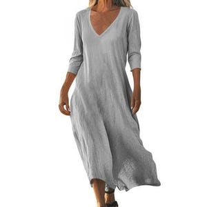May include: A light gray, V-neck dress with three-quarter sleeves. The dress has a loose, flowing design and falls to the mid-calf. The fabric appears to be a lightweight linen or cotton blend, suitable for warm weather.