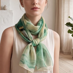 May include: A lightweight square scarf featuring a watercolor-inspired abstract pattern in shades of sage green, cream, and dark olive. The scarf is tied in a simple knot at the neck, showcasing a smooth, semi-sheer fabric with soft, flowing lines.