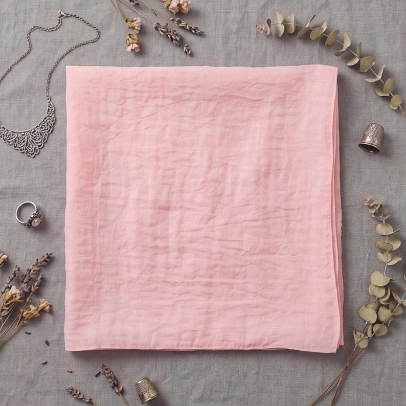 K&ouml;nnte beinhalten: Ein quadratisches, hellrosa Stofftuch mit knittriger Textur. Das Tuch ist umgeben von einer silbernen Filigrankette, einem Silberring, zwei kleinen Metall-Fingerh&uuml;ten, getrockneten Lavendelzweigen und einem Eukalyptuszweig auf grauem Untergrund.