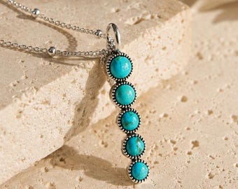 May include: A silver-toned necklace featuring a vertical pendant with five round, bright turquoise stones set in a beaded metal frame. The chain is a delicate link style with small, evenly spaced silver beads along the length of the necklace.