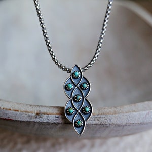 Puede incluir: Un collar de cadena de plata con un colgante que presenta un dise&ntilde;o geom&eacute;trico con piedras turquesa.