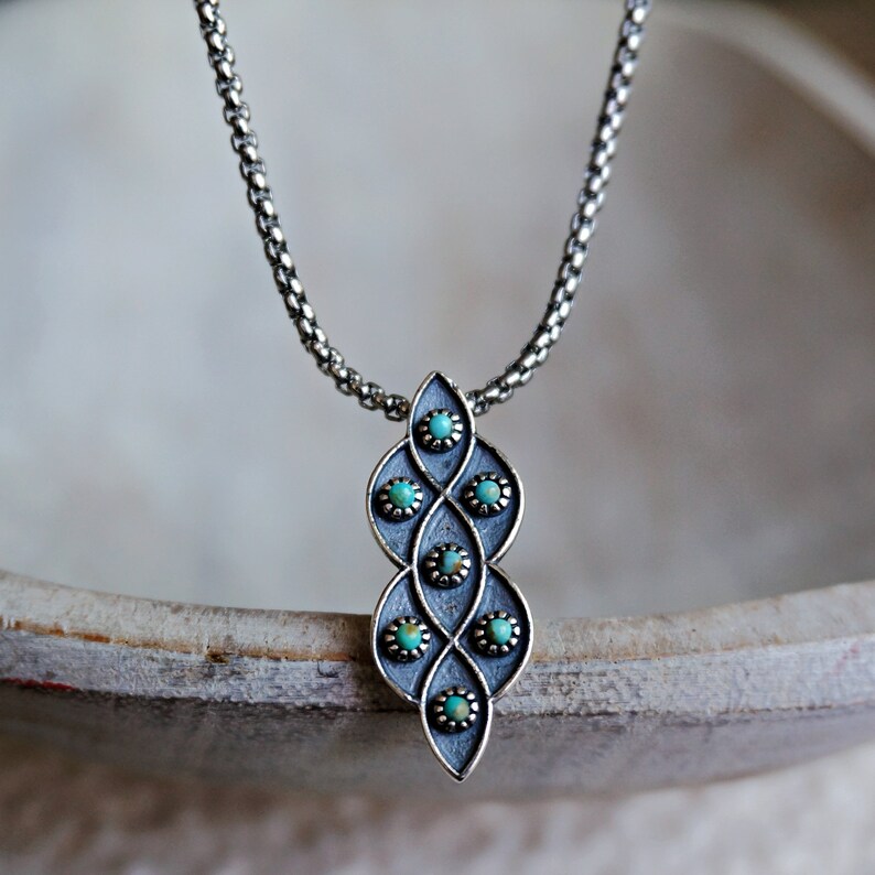 Puede incluir: Un collar de cadena de plata con un colgante que presenta un dise&ntilde;o geom&eacute;trico con piedras turquesa.
