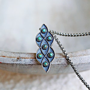 Puede incluir: Un collar de plata con un colgante de dise&ntilde;o de piedra turquesa. El colgante tiene forma de l&aacute;grima y presenta un patr&oacute;n repetitivo de piedras turquesas engastadas en plata.