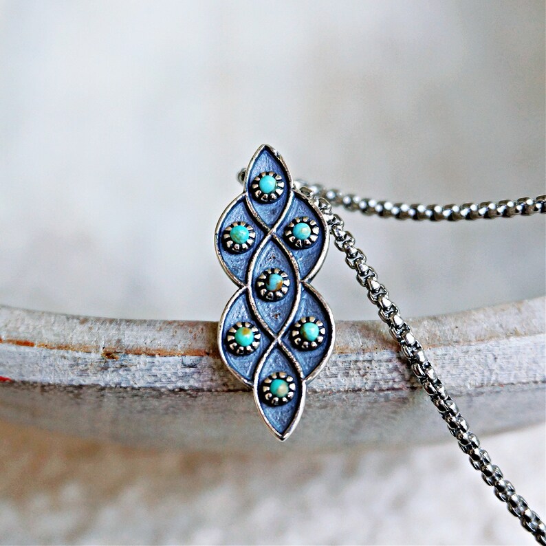 Puede incluir: Un collar de plata con un colgante de dise&ntilde;o de piedra turquesa. El colgante tiene forma de l&aacute;grima y presenta un patr&oacute;n repetitivo de piedras turquesas engastadas en plata.